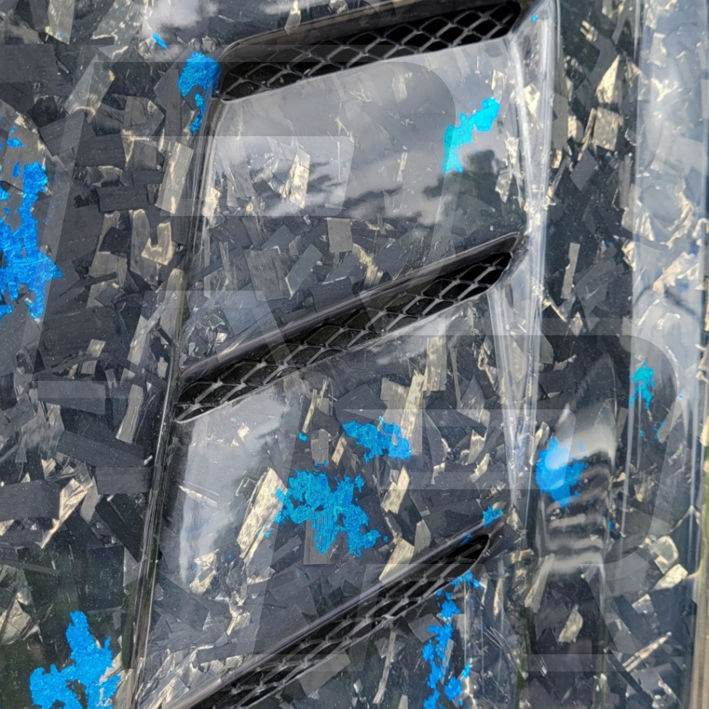 Close-up of a car's carbon fiber hood with vents and a textured black and blue background.